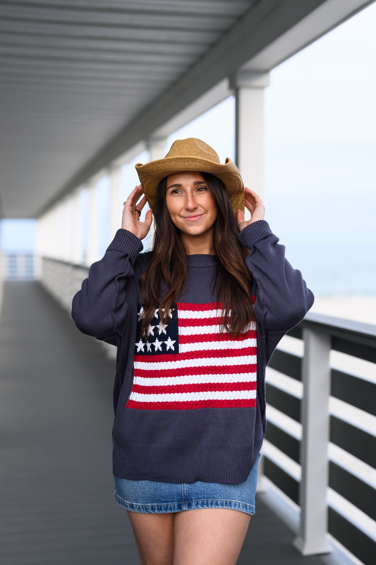 Woman wearing an American flag knit sweater from Crosswynds Traders on a porch overlooking the water in Narragansett, RI
