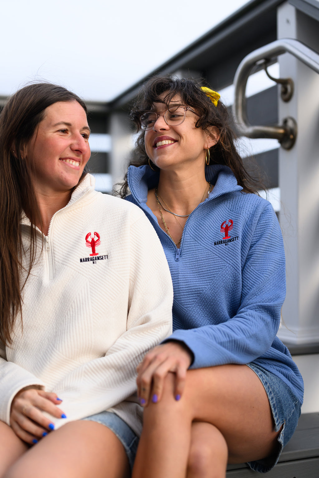 Two women laughing on a dock wearing Coastal Lobster Quarter Zip in vintage white and soft blue