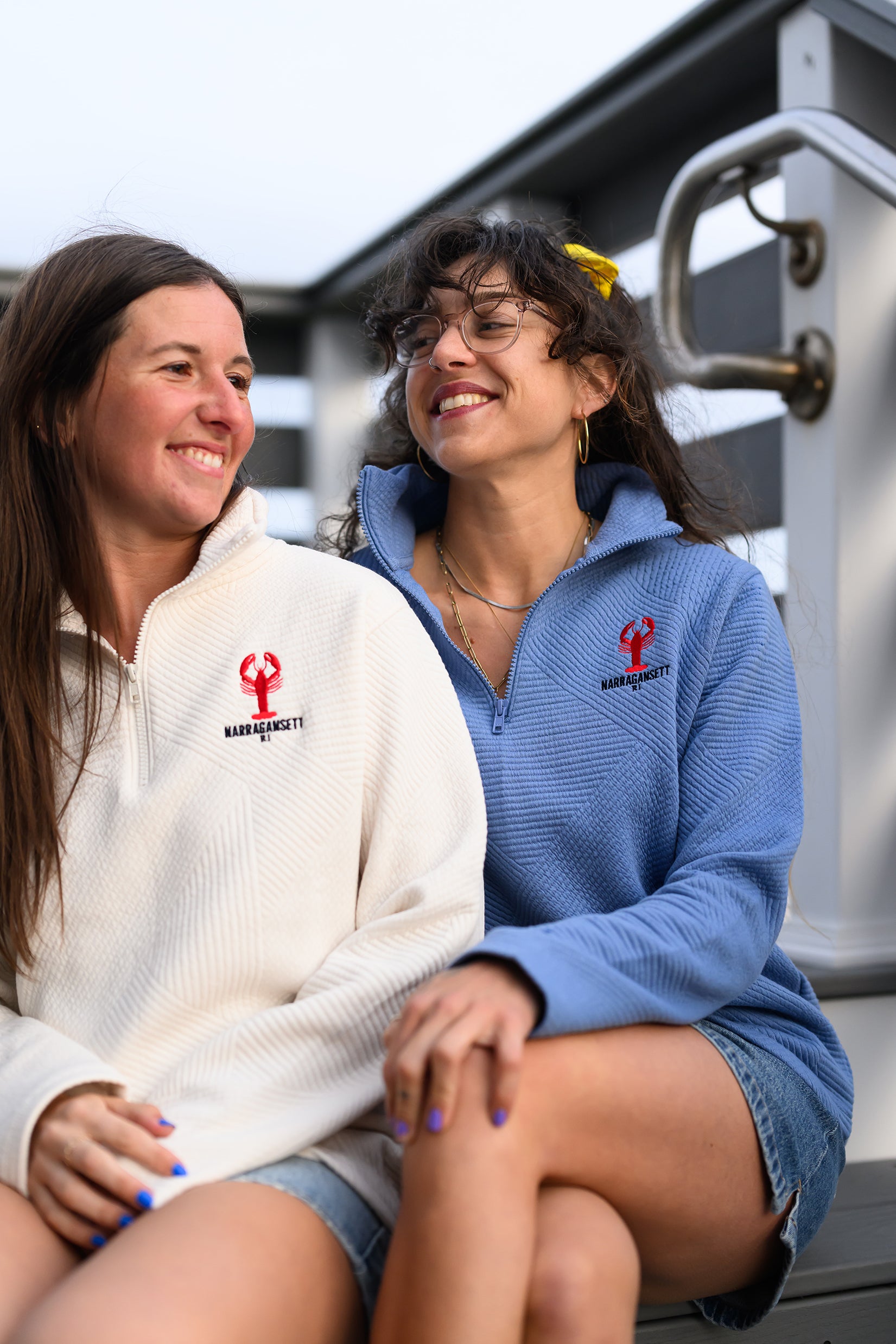 Two women laughing on a dock wearing Coastal Lobster Quarter Zip in vintage white and soft blue