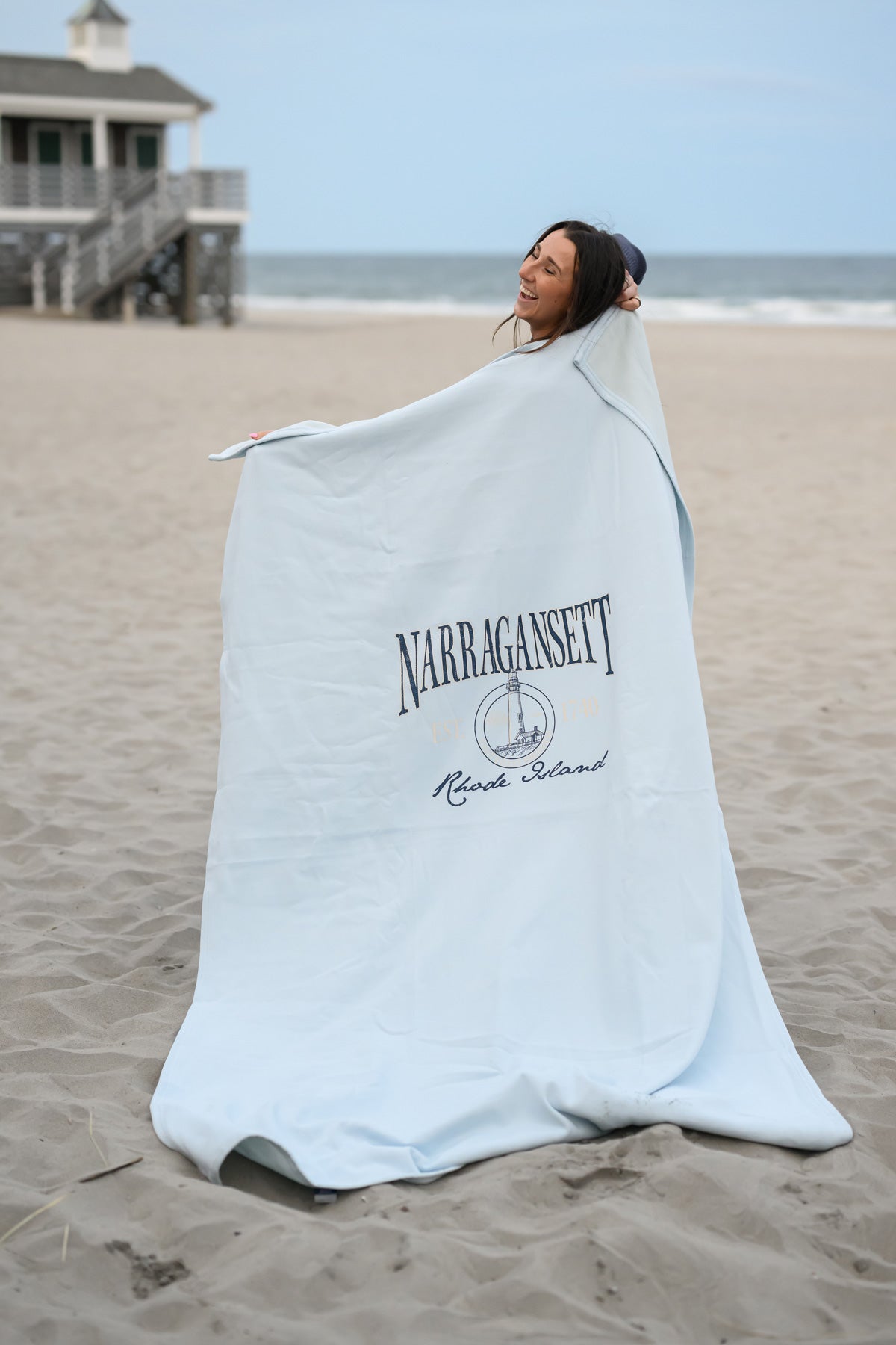 Woman wrapped in a Narragansett, Rhode Island lighthouse blanket on the beach

