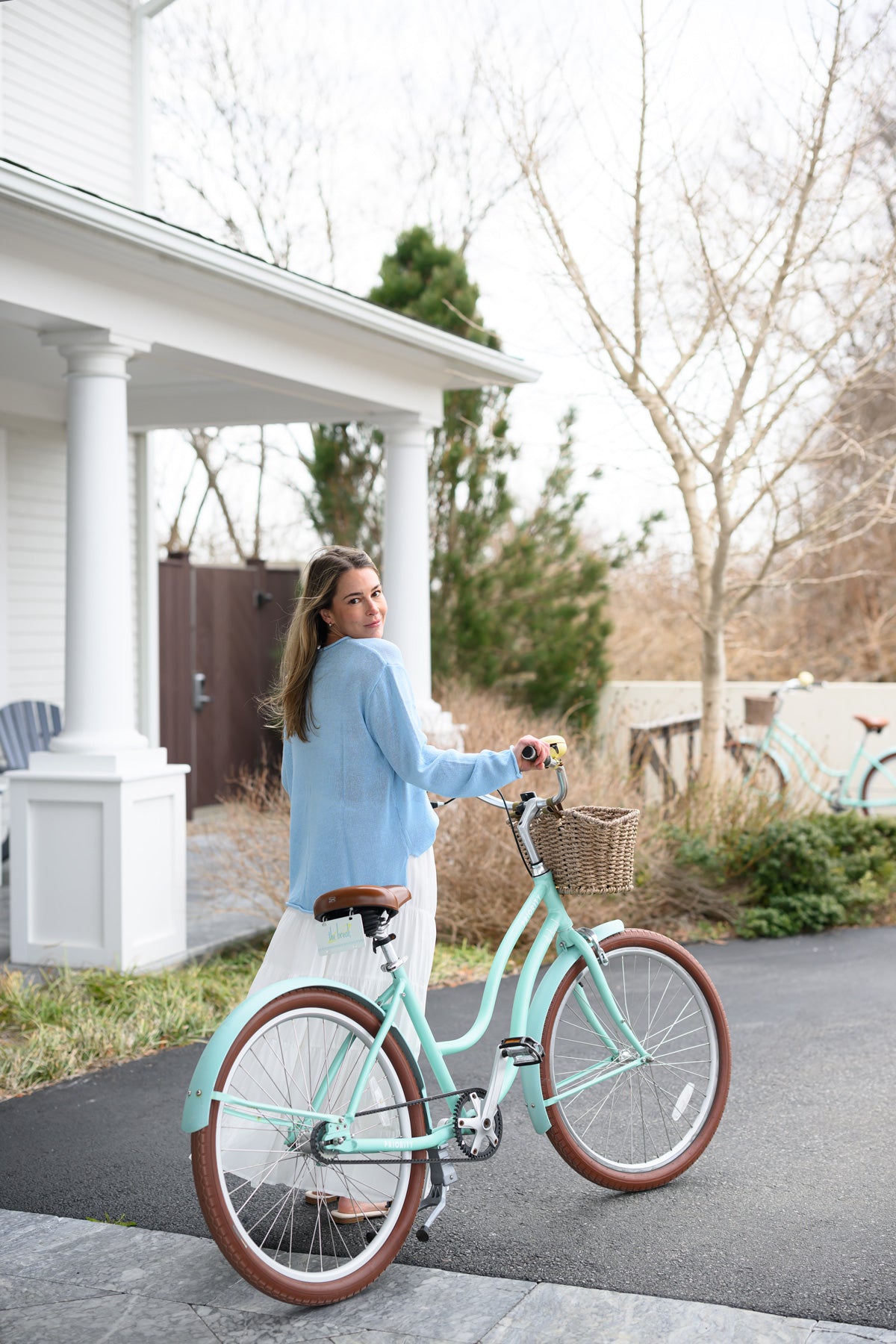 Woman in a light blue sweater and white skirt with a mint green bicycle outside The Break Hotel in Narragansett, RI