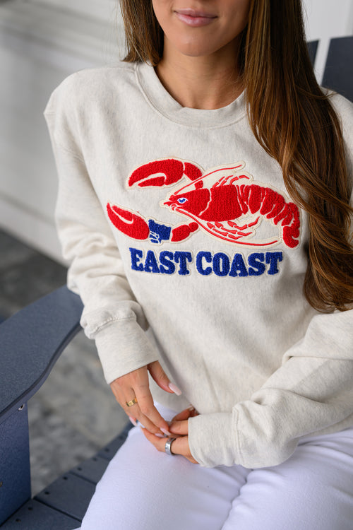 Person wearing a cream sweatshirt with a red lobster graphic and 'East Coast' text.